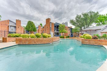 A swimming pool surrounded by a brick wall and residential buildings.